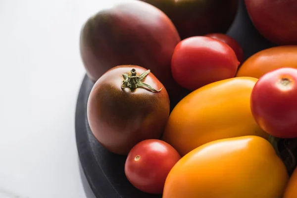 Close up view of red and yellow tomatoes on wooden pizza pan on marble surface — Stock Photo