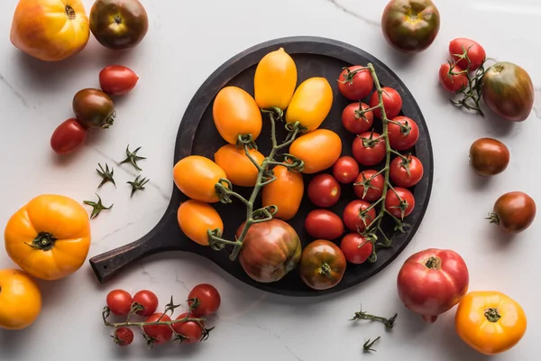 Draufsicht auf verschiedene gelbe, rote und Kirschtomaten auf Pizzapfanne auf Marmoroberfläche — Stockfoto