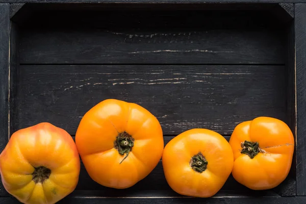 Vue de dessus de quelques tomates jaunes dans une boîte noire en bois — Photo de stock