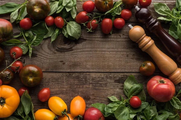 Top view of tomatoes, spinach, pepper mill, salt mill and empty space in middle on wooden table — Stock Photo