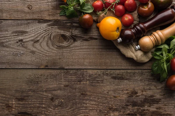 Vue de dessus des tomates et des épinards près du moulin à poivre et du moulin à sel sur un morceau de tissu sur une surface en bois — Photo de stock