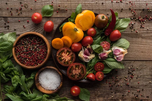 Top view of plate with spinach, garlic and sliced tomatoes near scattered pepper and bowls on wooden table — Stock Photo