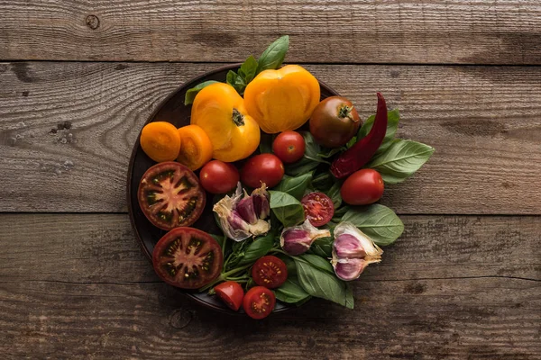 Top view of plate with spinach, garlic, chilli pepper and sliced tomatoes on wooden table — Stock Photo