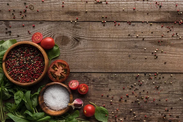 Top view of scattered pepper near sliced cherry tomatoes, spinach and bowls on wooden table — Stock Photo