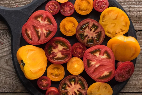 Top view of sliced red and yellow tomatoes on pizza pan on wooden table — Stock Photo