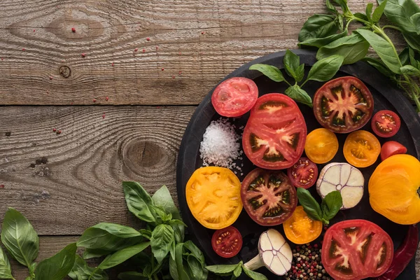 Top view of tomatoes, garlic, chilli pepper, salt and pepper on pizza pan near spinach on wooden table — Stock Photo
