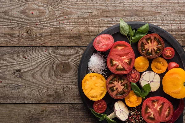 Top view of tomatoes, garlic, spinach, chilli pepper, salt and pepper on pizza pan on wooden surface — Stock Photo