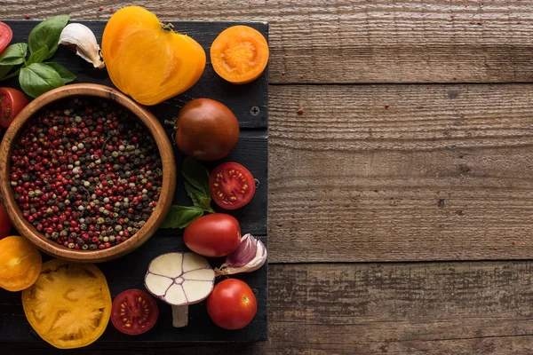 Vista superior da bandeja preta com pimenta na tigela, pimenta, tomates fatiados e alho na mesa de madeira — Fotografia de Stock