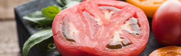 Panoramic shot of sliced red and yellow tomatoes with spinach on black tray on wooden table — Stock Photo