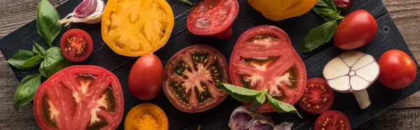 Panoramic shot of sliced yellow and cherry tomatoes with spinach, garlic and chilli pepper on black wooden tray — Stock Photo