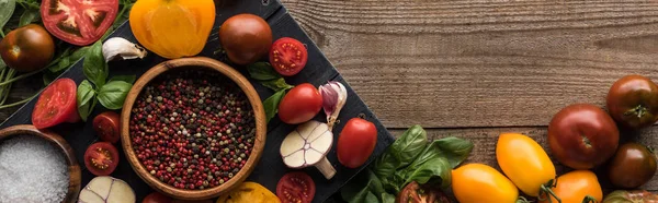 Tiro panorâmico de bandeja preta com pimenta e sal em tigelas, pimenta, tomates fatiados e alho perto de legumes espalhados na mesa de madeira — Fotografia de Stock