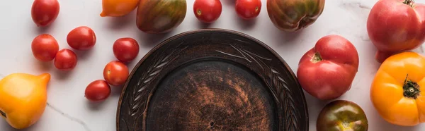 Panoramic shot of empty wooden plate near scattered tomatoes on white marble surface — Stock Photo