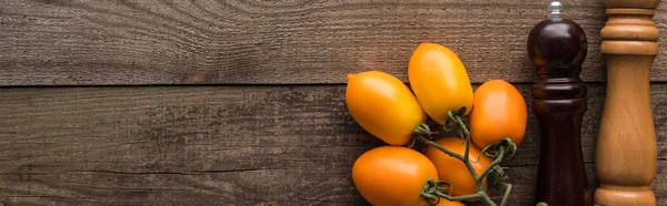 Tiro panorâmico de tomates amarelos perto do moinho de pimenta e moinho de sal na mesa de madeira — Fotografia de Stock