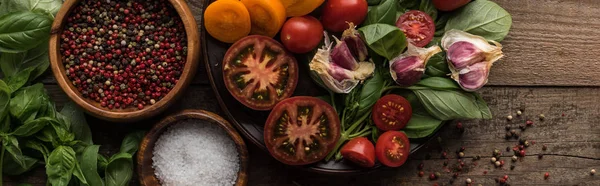 Plano panorámico de plato con espinacas, ajo y tomates en rodajas cerca de pimiento disperso y cuencos en mesa de madera - foto de stock