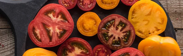 Panoramic shot of sliced red and yellow tomatoes on pizza pan on wooden table — Stock Photo