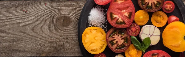 Панорамный снимок помидоров, чеснока, шпината, перца чили, соли и перца на сковороде для пиццы на деревянном столе — стоковое фото