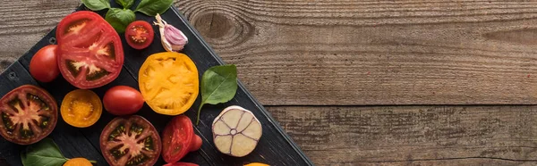 Panoramic shot of tomatoes, garlic, spinach on tray on wooden table — Stock Photo