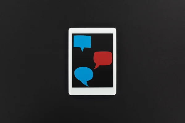 Vista superior de la tableta digital con burbujas vacías de habla roja y azul sobre fondo negro, concepto de acoso cibernético - foto de stock