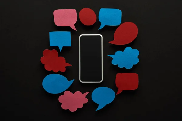 Top view of smartphone with blank screen on black background with empty speech bubbles, cyberbullying concept — Stock Photo