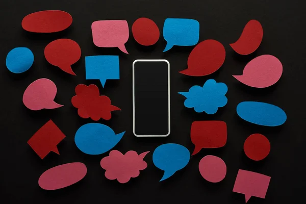 Ansicht von Smartphone mit leerem Bildschirm auf schwarzem Hintergrund mit leeren roten und blauen Sprechblasen, Cybermobbing-Konzept — Stockfoto