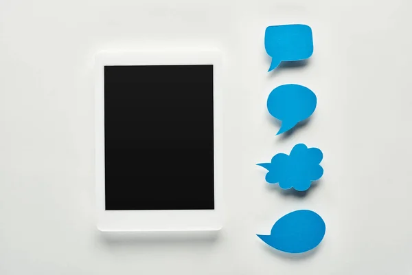 Top view of digital tablet with blank screen on white background near empty blue speech bubbles, cyberbullying concept — Stock Photo