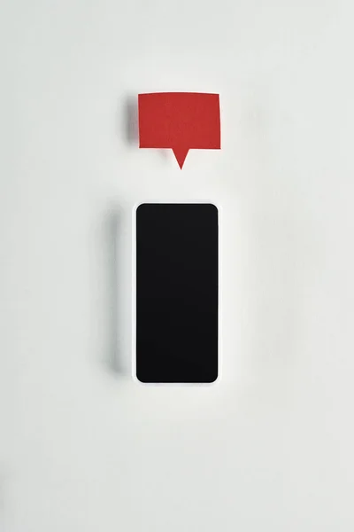 Vista dall'alto dello smartphone con schermo bianco su sfondo bianco con bolla vocale vuota rossa sopra, concetto di cyberbullismo — Foto stock