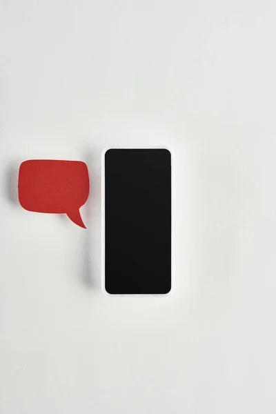 Top view of smartphone on white background near red empty speech bubble, cyberbullying concept — Stock Photo