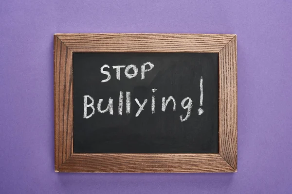 Top view of chalkboard in wooden frame with stop bullying lettering on purple background — Stock Photo