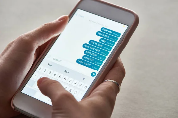 Cropped view of abuser sending offensive messages while using smartphone, illustrative editorial — Stock Photo