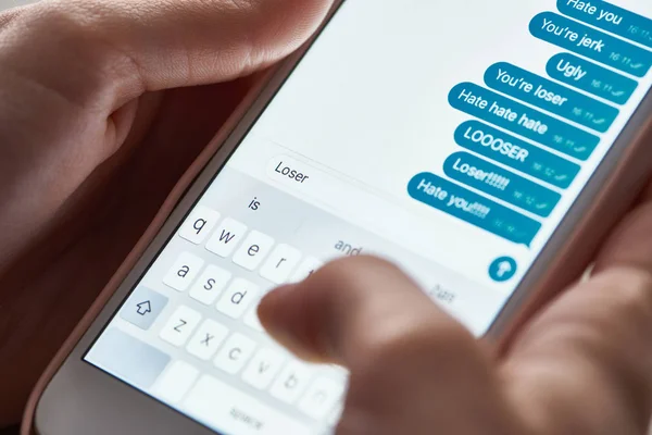 Partial view of abuser sending offensive messages while using smartphone, illustrative editorial — Stock Photo