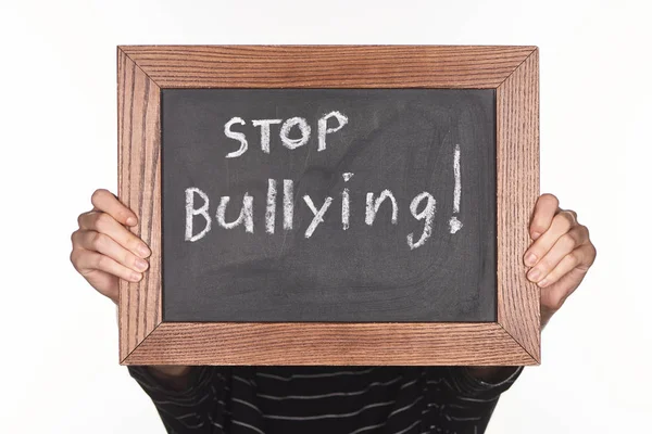 Niña sosteniendo pizarra en marco de madera con letras de stop bullying aislado en blanco - foto de stock