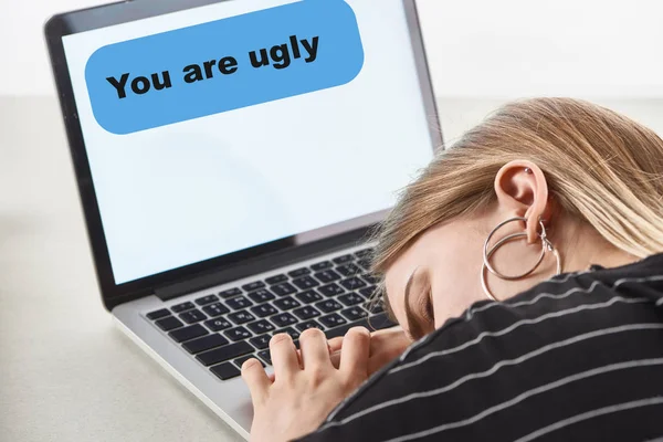 Chica rubia durmiendo cerca del ordenador portátil con usted son mensaje feo en la pantalla, concepto de acoso cibernético - foto de stock