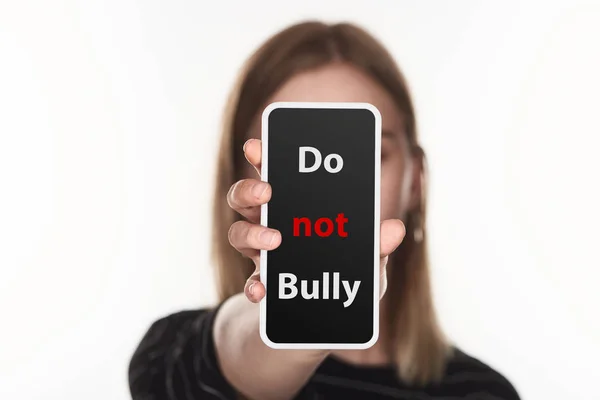 Enfoque selectivo de la víctima de acoso cibernético que muestra el teléfono inteligente con no bully letras en la pantalla aislada en blanco - foto de stock