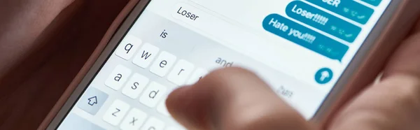 Panoramic shot of abuser typing offensive messages while using smartphone, illustrative editorial — Stock Photo