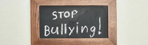 Panoramic shot of chalkboard in wooden frame with stop bullying lettering on grey background — Stock Photo