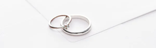 Panoramic shot of silver wedding rings on white envelope — Stock Photo