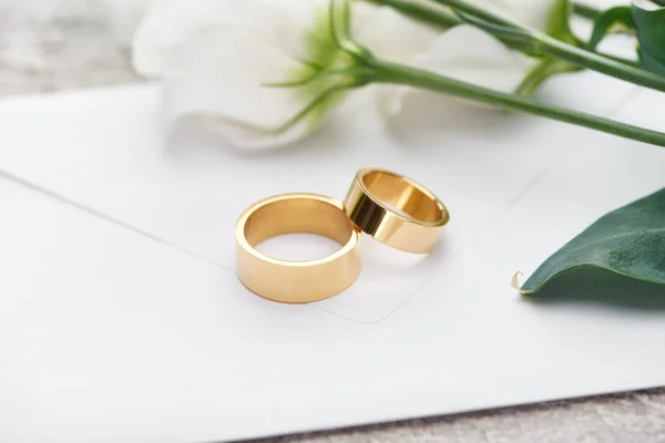 Golden wedding rings on white envelope near white flowers — Stock Photo