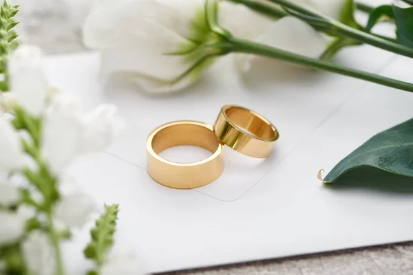 Selective focus of wedding rings on white envelope near white eustoma flowers — Stock Photo