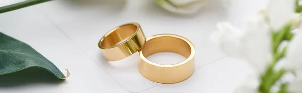 Selective focus of golden wedding rings on white envelope, panoramic shot — Stock Photo