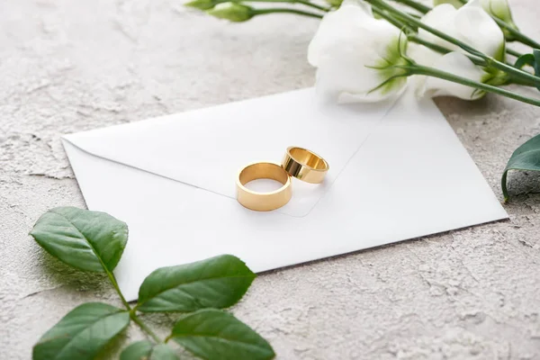 Anillos de oro en sobre blanco cerca de flores eustoma en textura gris - foto de stock