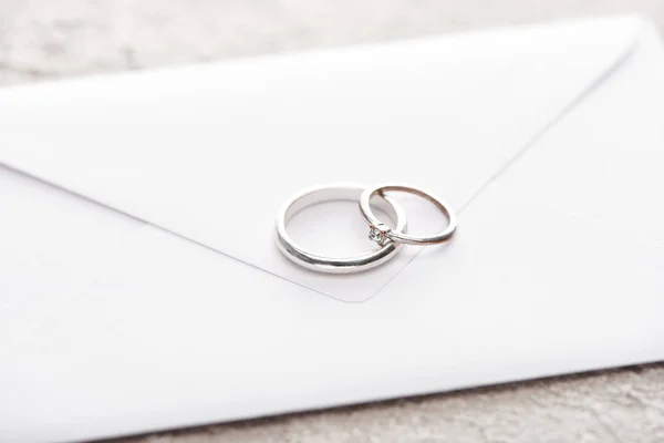 Silver wedding rings on white envelope on grey textured surface — Stock Photo