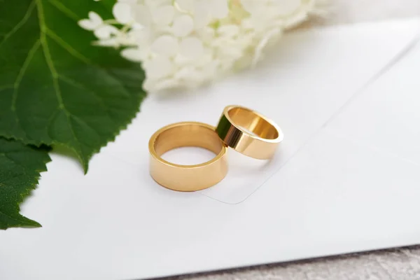 Золотые обручальные кольца на белом конверте рядом с гортензивным цветком — Stock Photo