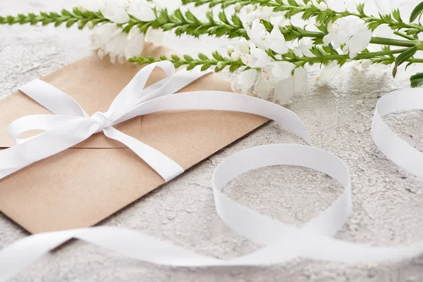 Selective focus of beige envelope with ribbon near white flowers on textured surface — Stock Photo