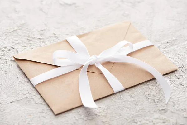 Бежевый конверт с белой лентой на серой текстурированной поверхности — стоковое фото