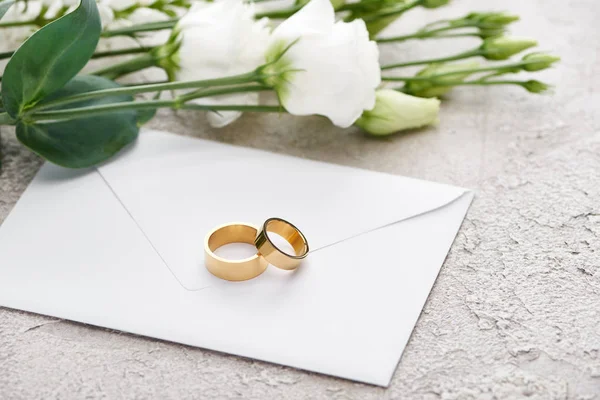 Golden wedding rings on envelope near white eustoma flowers on textured surface — Stock Photo