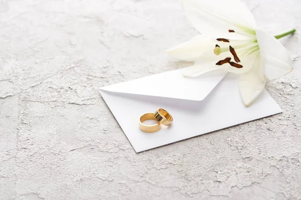 Dos anillos de boda de oro en el sobre cerca de lirio blanco en la superficie texturizada - foto de stock