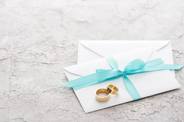 Dos anillos dorados sobre sobres blancos con cinta azul sobre superficie texturizada - foto de stock