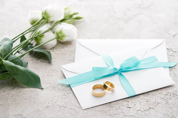Golden rings on white envelopes with ribbon near eustoma flowers on textured surface — Stock Photo