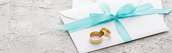 Panoramic shot of golden rings on white envelope with blue ribbon — Stock Photo