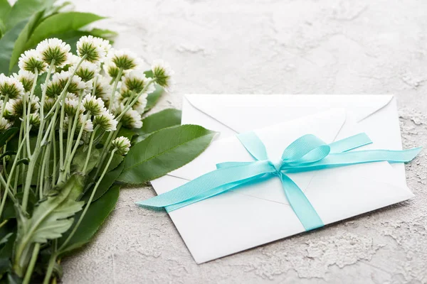 White envelopes with blue ribbon near chrysanthemums on grey textured surface — Stock Photo